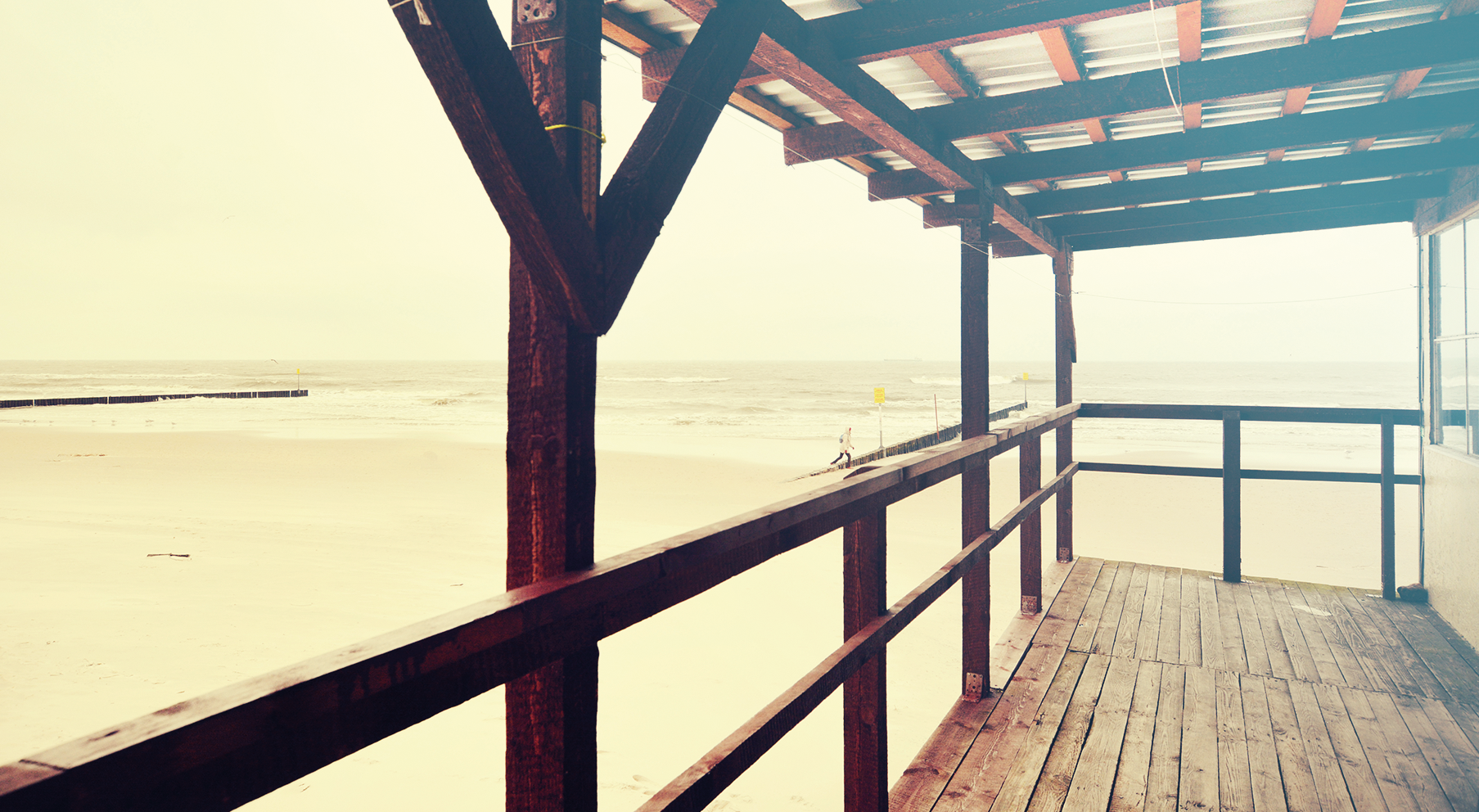 Holzsteg zum Sandstrand mit Meerblick und hellem Himmel.